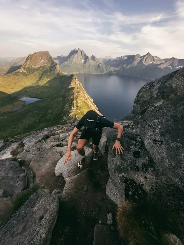 Mountain athlete scrambling over rocks to a summit above a fjord