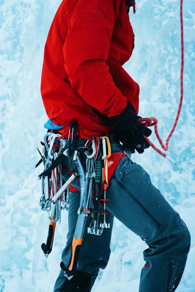 Ice climber in a red jacket with ice tools and climbing gear on an ice wall